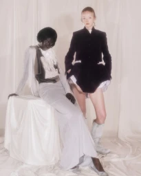 Lily Nova and a model posing in draped and tailored garments against a cream fabric backdrop.