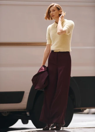 A stylish adult female in fashionable outerwear with high heels poses against a neutral van, offering a modern, urban aesthetic.