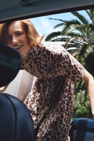 Woman in a leopard print dress leaning into a car, with palm trees visible in the background