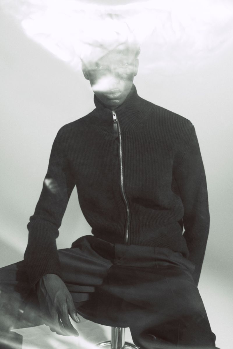 Model Baba Diagne in a dark zip-up jacket seated against a light background for Maison Margiela.