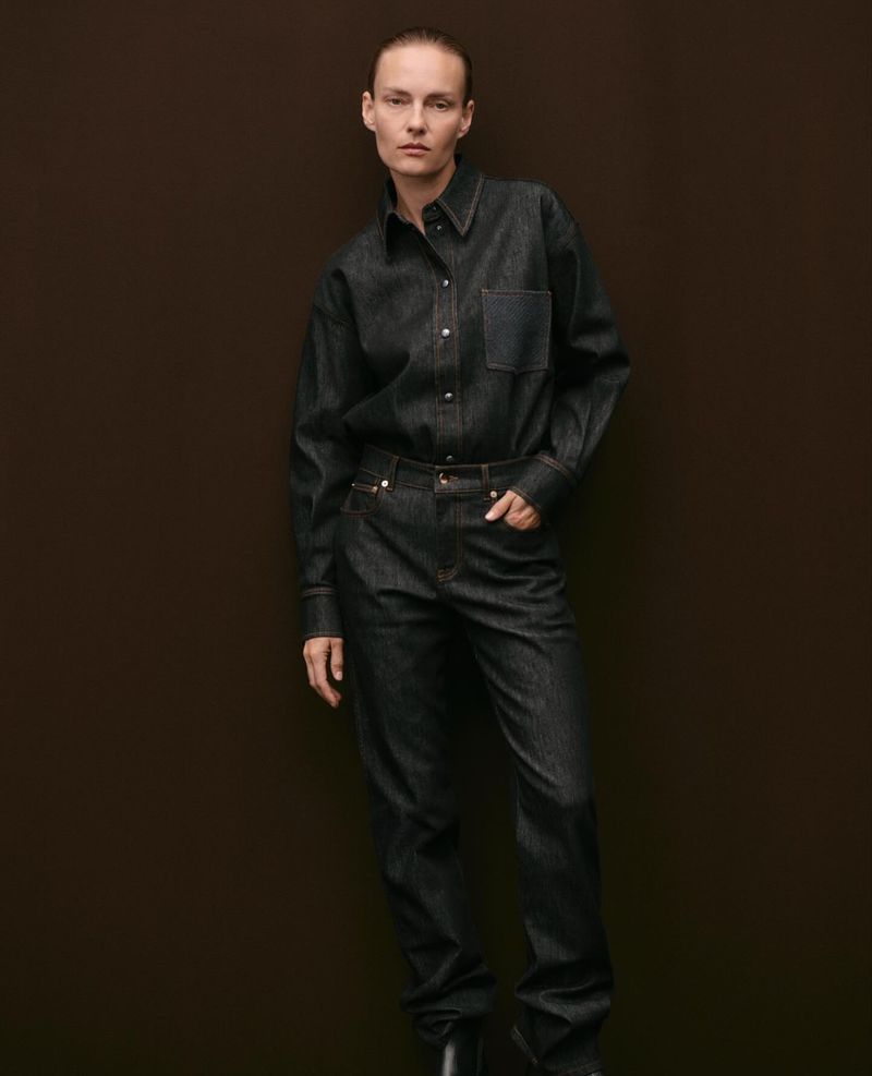 Model Ania Kisiel wearing a dark raw denim shirt and matching jeans against a solid dark brown backdrop.