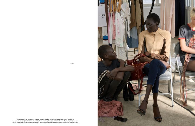 Two dark-skinned women sit in chairs next to a clothing rack, one wearing a brown suede jacket, dark jeans, and heels, inside.