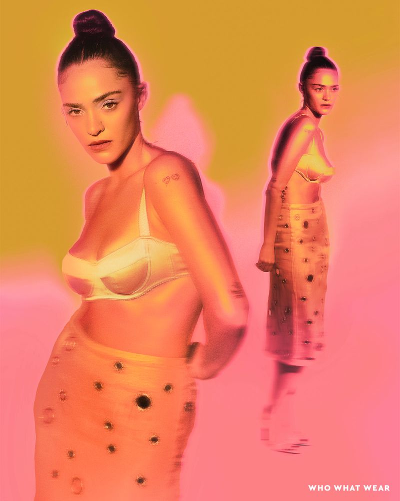 Actor Luna Blaise poses in a pale bralette and embellished skirt amidst glowing pink and yellow tones.