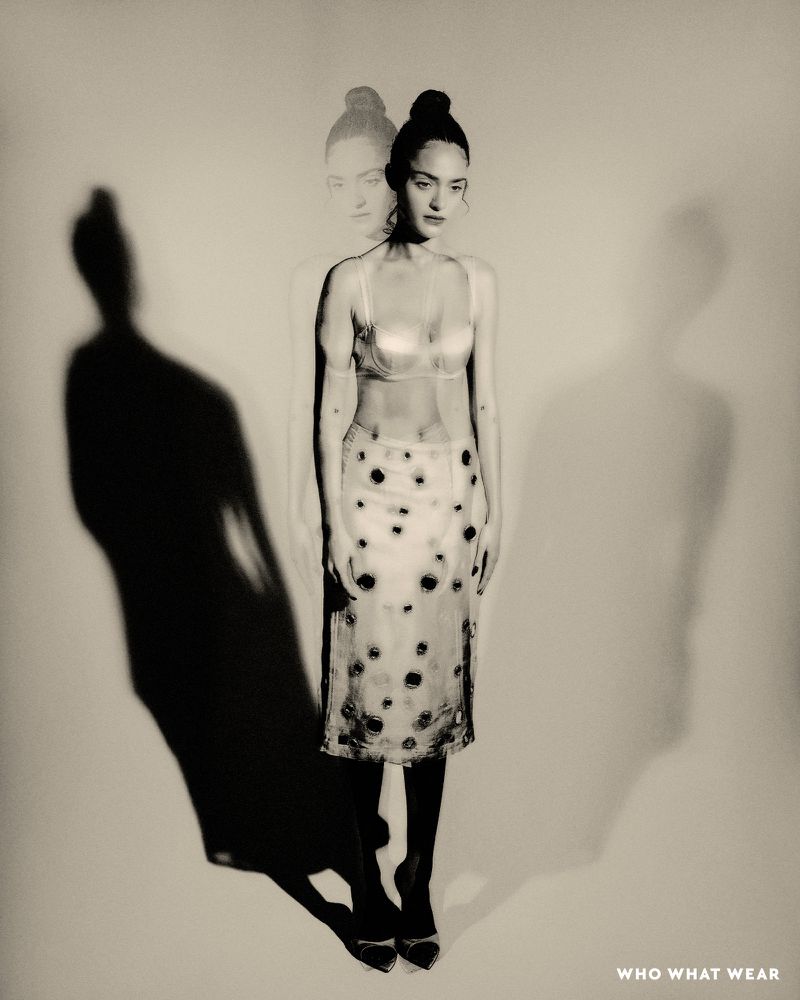 Monochrome studio shot of a young adult woman in a bra top and skirt, accompanied by shadow and ghosting effects, posing gracefully.