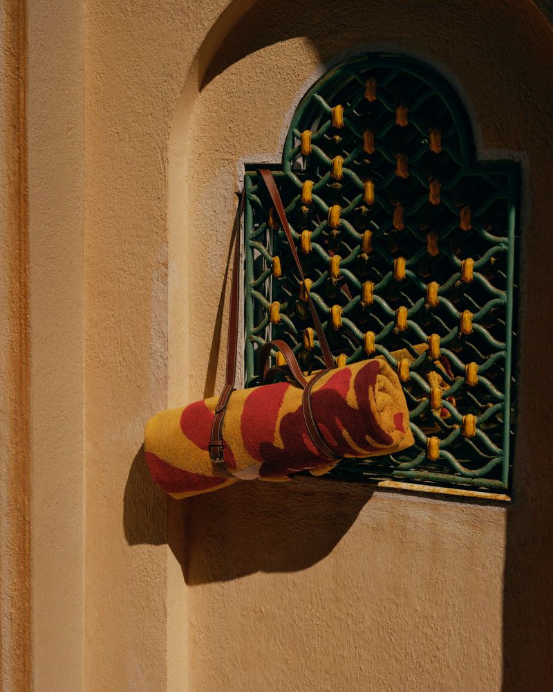 Rolled yellow and red patterned towel in a brown leather carrier strap hanging against a decorative green latticed window.