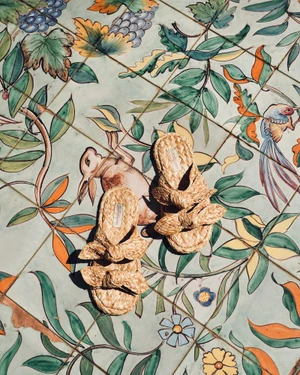 Pair of woven raffia bow slide sandals resting on ornate painted ceramic floor tiles under bright sunlight.