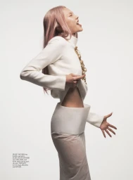 Model Hoyeon Jung with pink hair poses in profile wearing a sculptural white top and skirt against a bright white background.