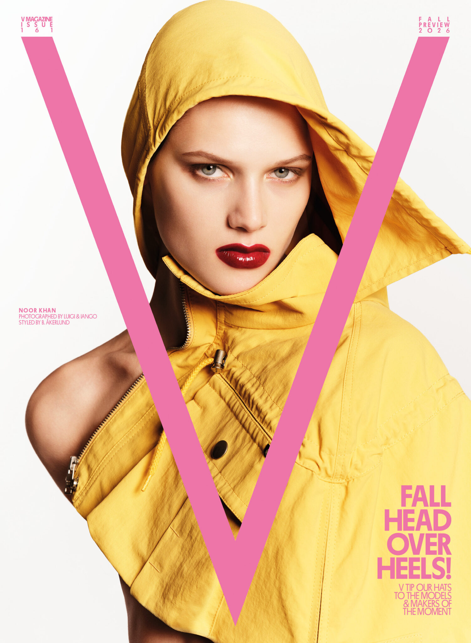 Model Noor Khan wearing a bright yellow hooded jacket with bold red lipstick against a white studio background with a pink V overlay.