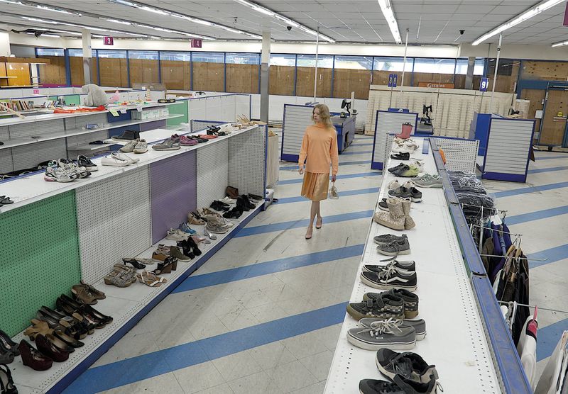 A blonde model in a peach top and pleated skirt walks down the shoe aisle of a spacious discount retail store.