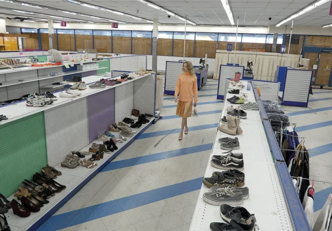 A blonde model in a peach top and pleated skirt walks down the shoe aisle of a spacious discount retail store.