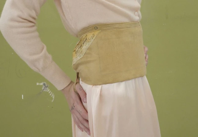 Close-up of a model wearing a pale pink cardigan, satin skirt, and a wide tan fabric heat wrap waist accessory.