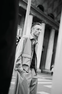 Model Joel Frampton wearing a grey utility jacket and matching trousers on a city street with classical columns.