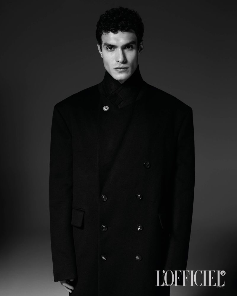 Model Leandro da Silva wearing a structured black double-breasted coat in a monochrome studio portrait for L'Officiel Hommes Italia.