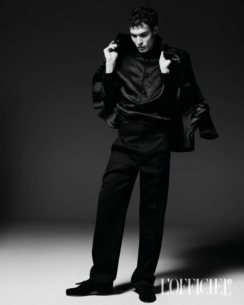 Monochrome fashion portrait of a male model wearing black suit and shirt against a dark background