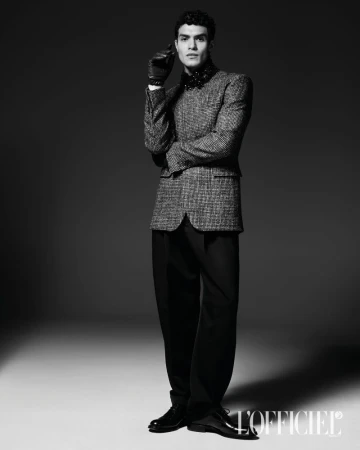 Model Leandro da Silva wearing a textured blazer, black trousers, and gloves in a monochrome studio portrait.