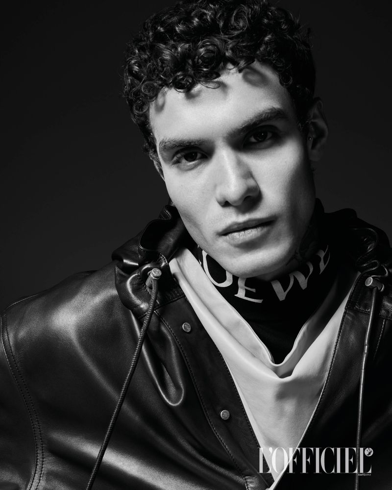 Black and white portrait of a man with curly hair wearing a hooded leather jacket for L'Officiel Hommes Italia.