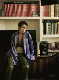 Model Lando van der Schee seated in a purple satin coat and olive trousers in front of a bookshelf.