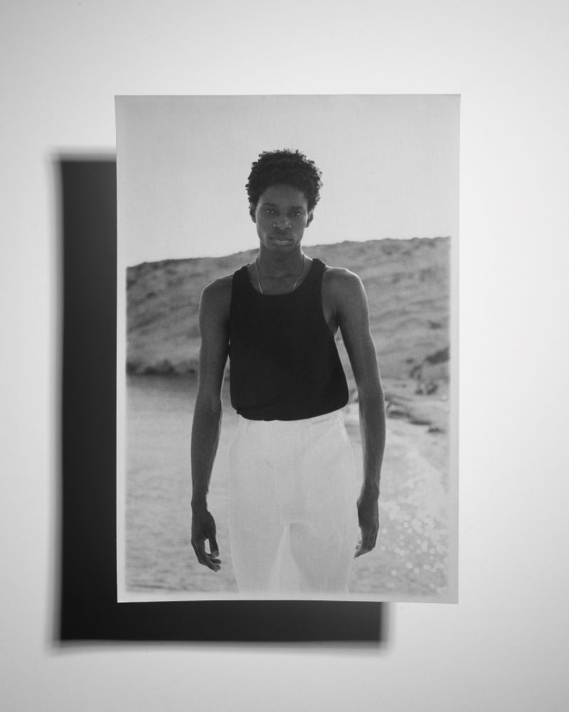 Monochrome photograph of a young adult standing in front of a body of water, with a shadow from a black card on the left.