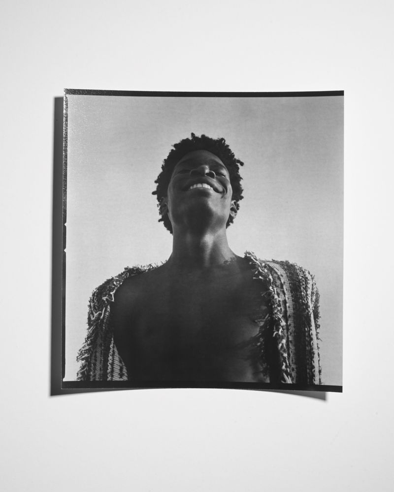 Monochrome portrait of smiling African American adult male looking up, wearing a textured jacket against a light background.