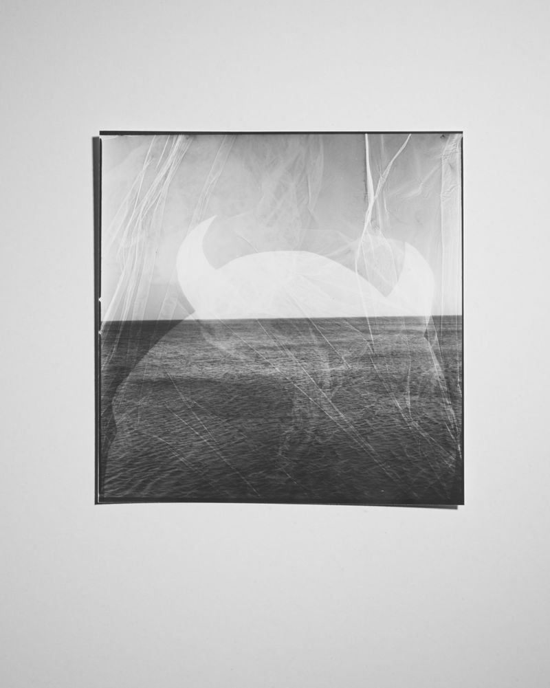 Monochrome photograph of a framed image featuring a white shape and dark water against a light background, creating an abstract composition.