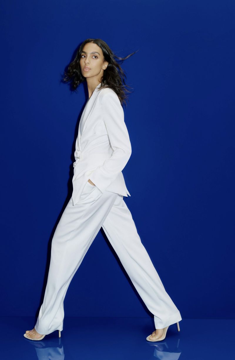 Model in a white pantsuit walking against a vibrant solid blue background for Veronica Beard Resort 2027 lookbook.