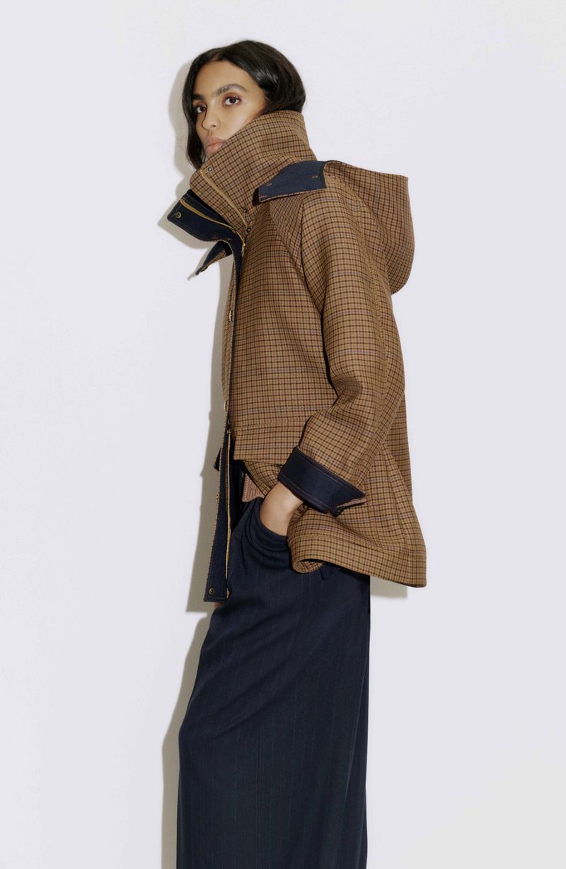 Model Noemi Kassa wearing a brown micro-check hooded jacket and navy wide-leg trousers against a clean white backdrop.