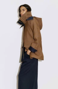 Model Noemi Kassa wearing a brown micro-check hooded jacket and navy wide-leg trousers against a clean white backdrop.