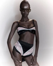 Model wearing dark shield sunglasses and a black high-waisted lace bikini set against a neutral studio backdrop.