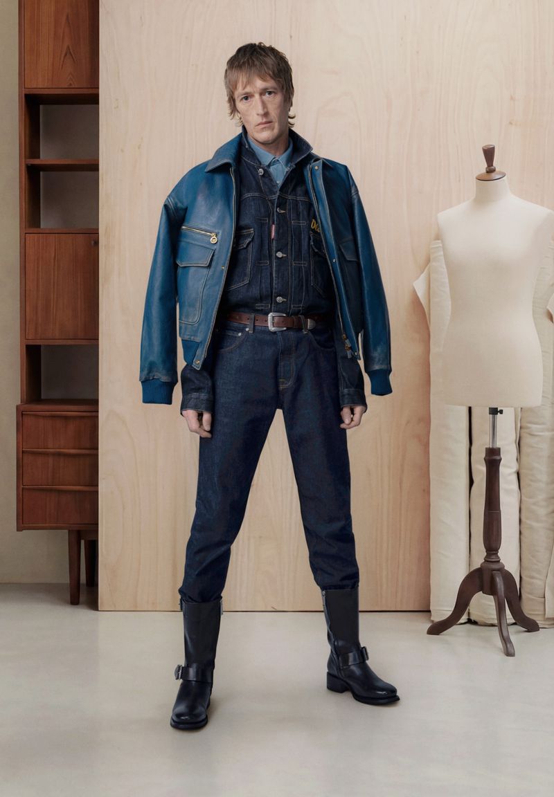 Model Thomas Westcott wearing a double denim outfit and blue leather jacket beside a mannequin in a studio setting.