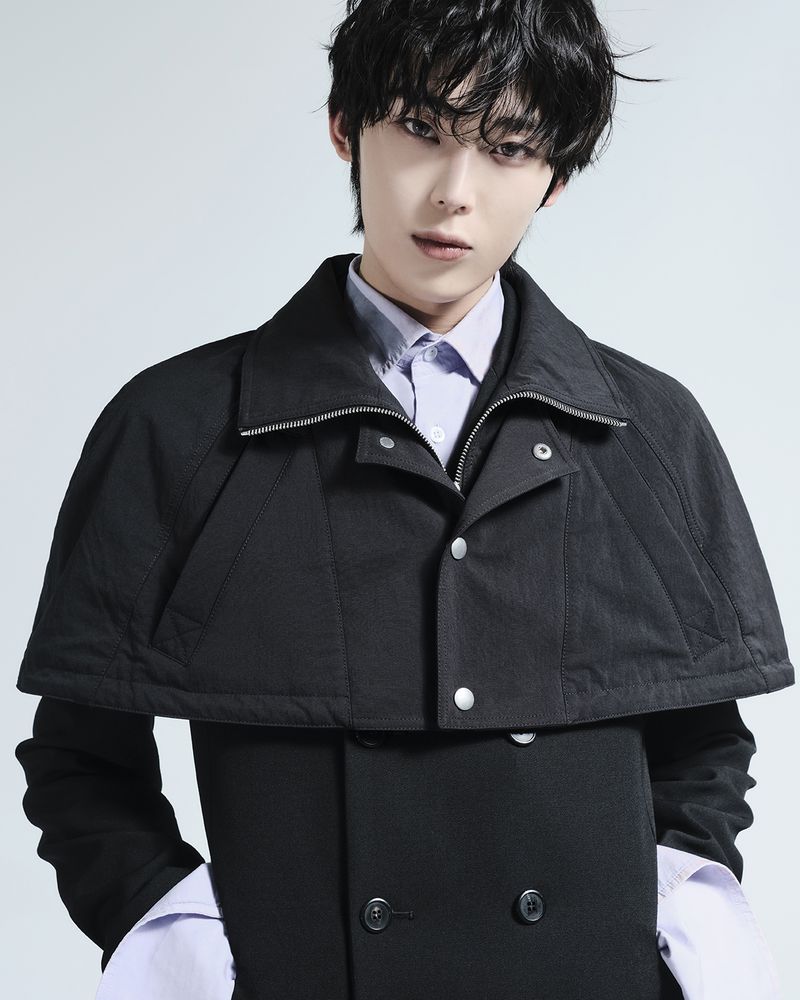 Young man wearing a black collared coat over a light purple shirt against a white background
