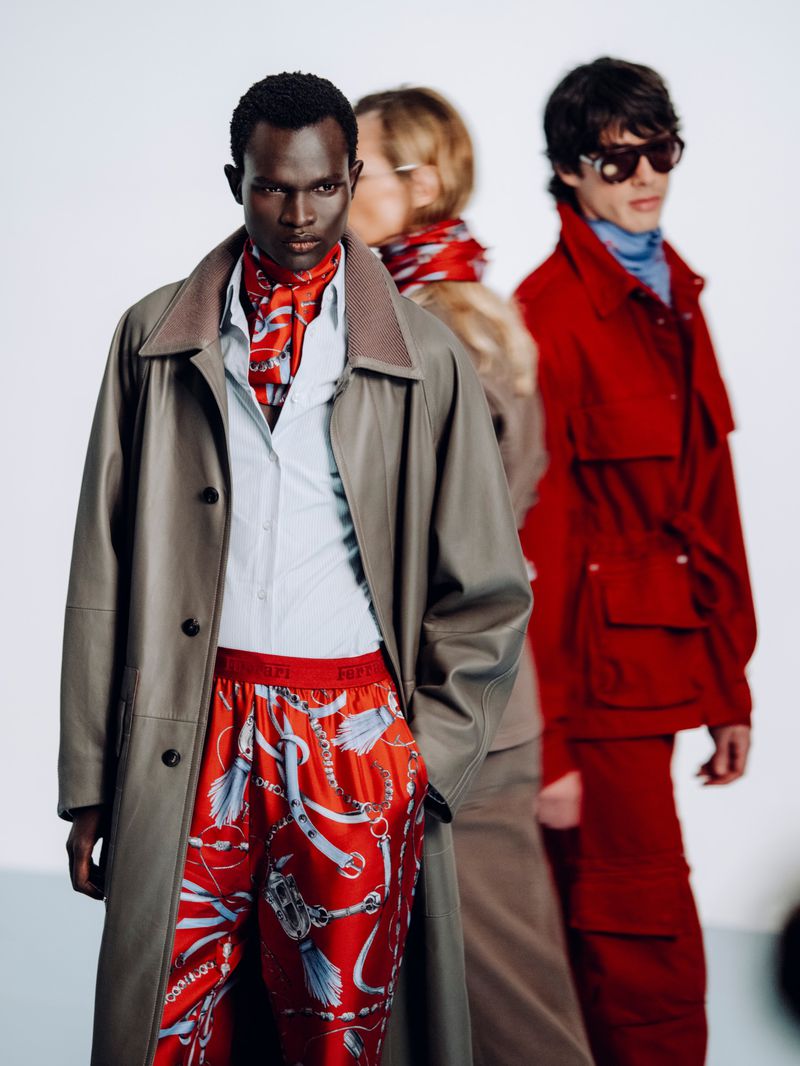 Model Chubath Kutien in a taupe leather coat and red patterned trousers posing in a studio for Ferrari Spring/Summer 2026.