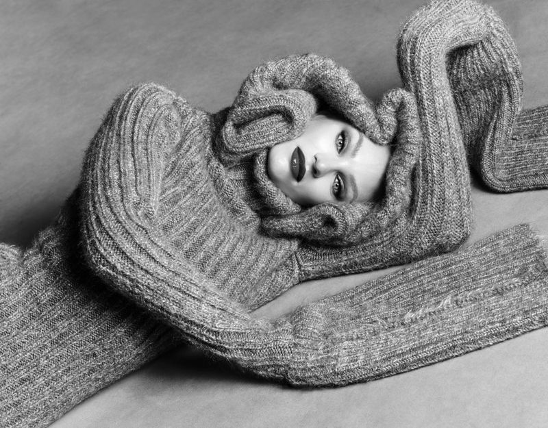 Candice Swanepoel lying down enveloped in an oversized ribbed knit sweater in a black and white fashion portrait.