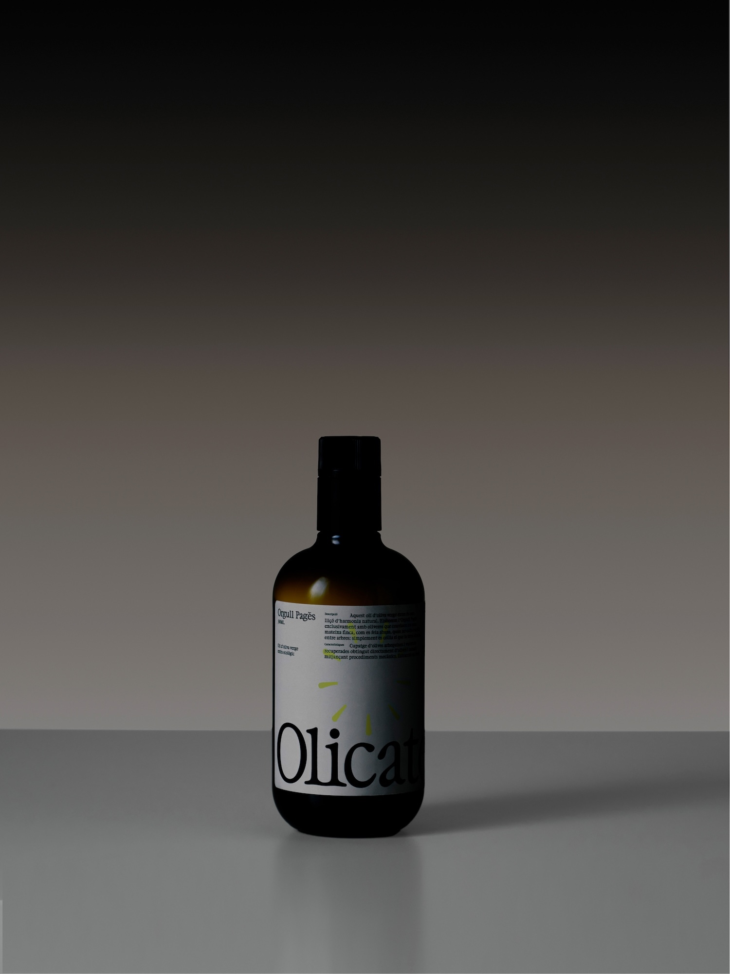 Olicatessen dark glass bottle with a white typographic label standing on a reflective surface against a dark gradient background.
