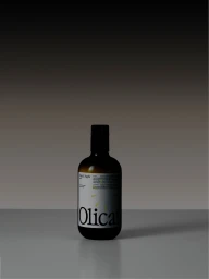 Olicatessen dark glass bottle with a white typographic label standing on a reflective surface against a dark gradient background.