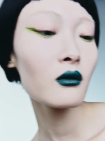 Close-up beauty portrait of model Zuoye with graphic green winged eyeliner, dark teal lipstick, and short black hair.
