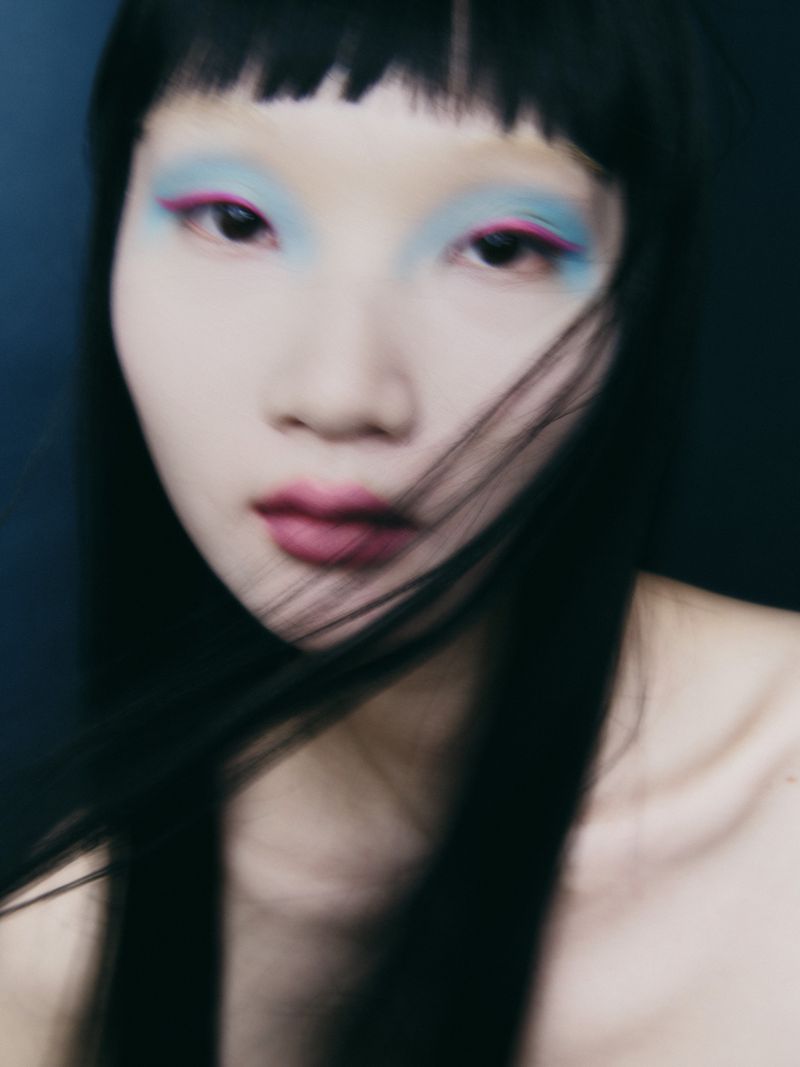 Close up portrait of a woman with vibrant blue eyeshadow, pink eyeliner, and long dark hair against a dark background.