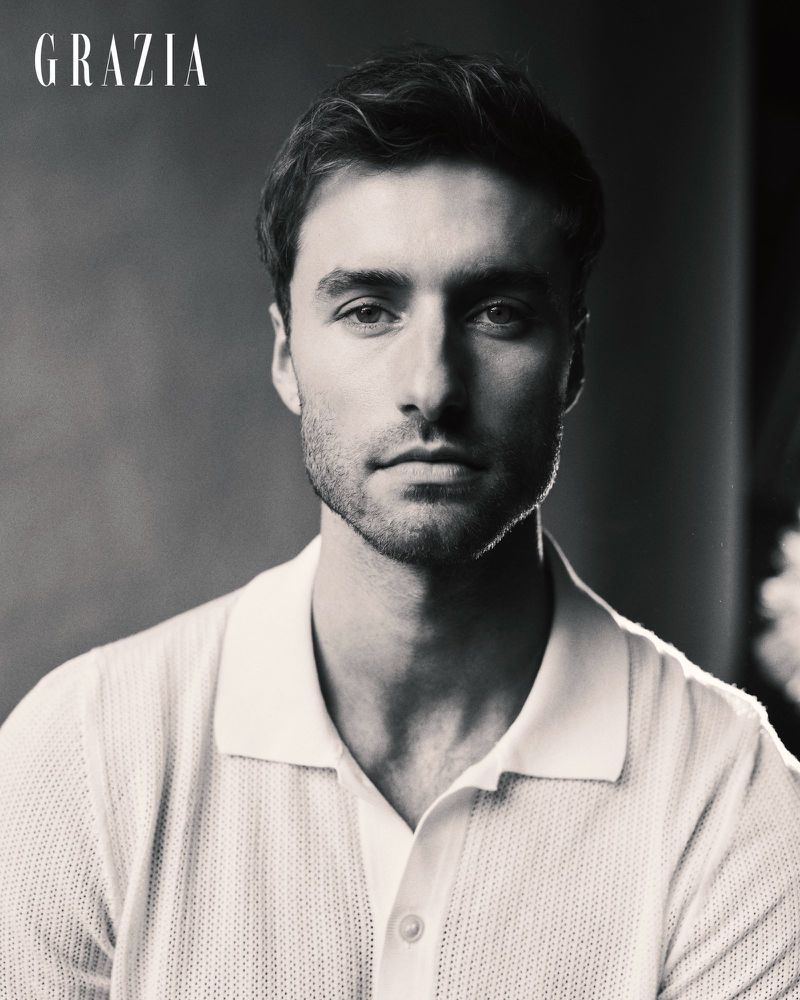 Black and white portrait of a man wearing a light-colored knit polo shirt against a neutral studio backdrop.