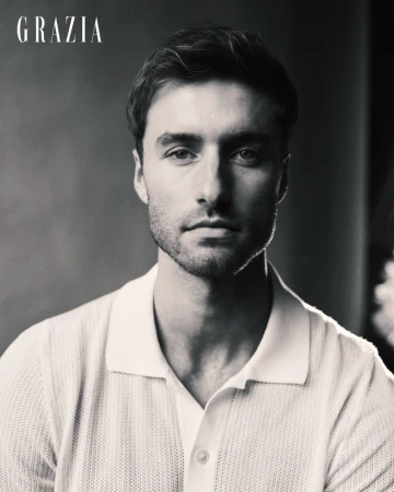 Black and white portrait of a man wearing a light-colored knit polo shirt against a neutral studio backdrop.