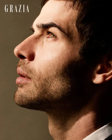 Close-up side profile portrait of a man with dark hair and stubble looking upward against a solid neutral studio backdrop.