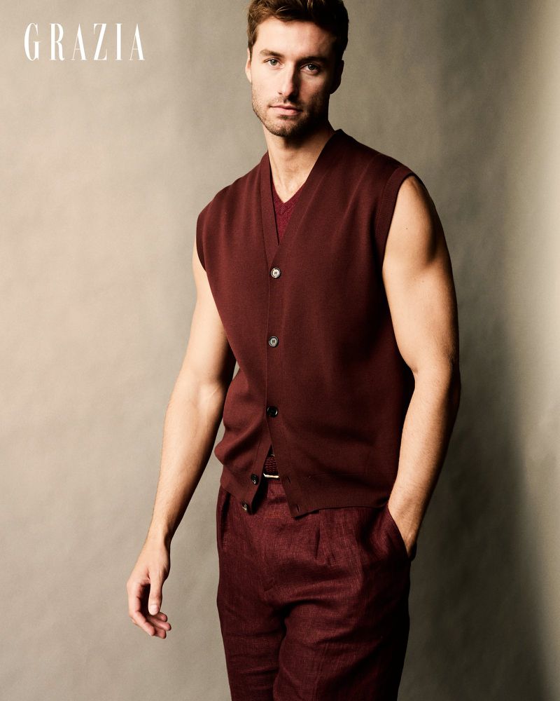 Man in a sleeveless burgundy knit vest and matching burgundy trousers posing against a neutral studio backdrop.
