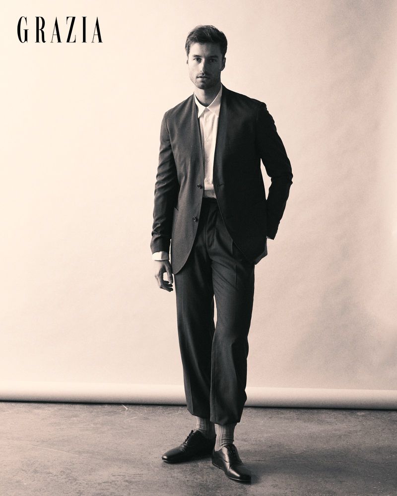 Man standing in a dark suit with cropped trousers and black dress shoes against a studio backdrop for Grazia Bulgaria.