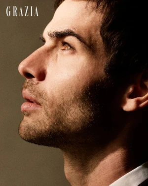 Close-up side profile portrait of a man with dark hair and stubble looking upward against a solid neutral studio backdrop.