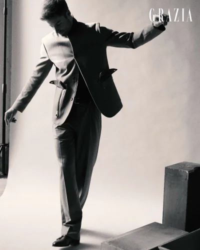 Man in a tailored suit posing dynamically with outstretched arms in a studio setting with pedestals.