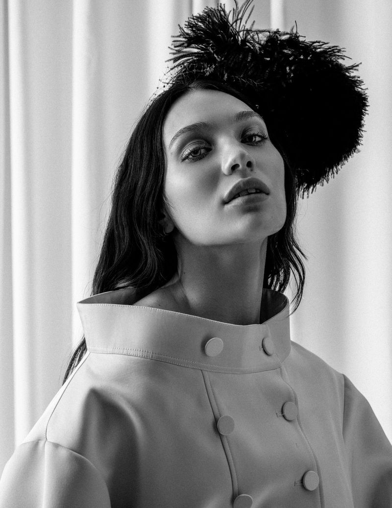 Portrait of Maddie Ziegler wearing a high-collared jacket and dark feathered headpiece against pleated curtains