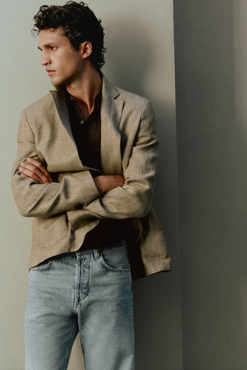 Francisco Henriques posing with arms crossed wearing a tan blazer and light blue jeans against a neutral wall.