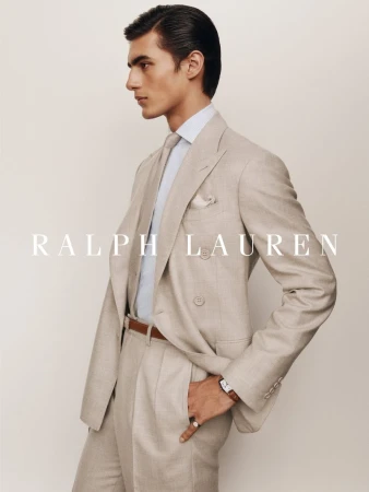 Male model in a tailored beige double-breasted suit, matching tie, and light blue shirt against a neutral off-white background.