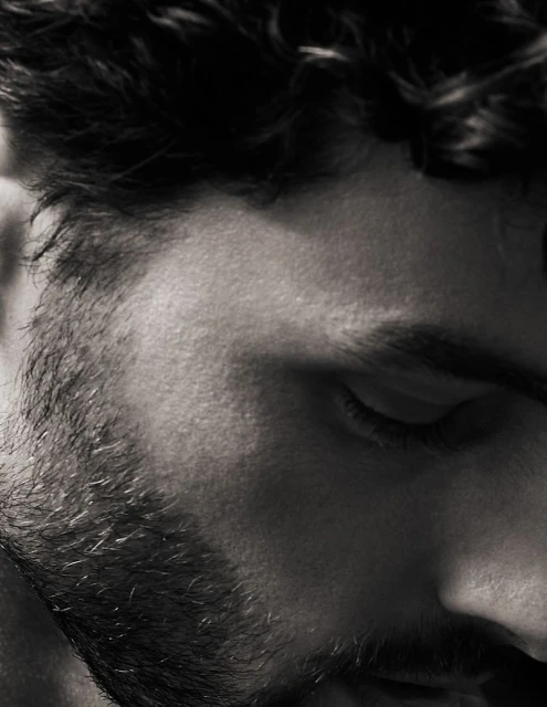 Monochrome close-up of a bearded man's face featuring his eyes closed, and focusing on his textured beard and curly dark hair.