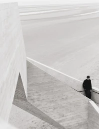 Model Hannes Gobeyn in black clothing leaning against a geometric concrete staircase overlooking an expansive sandy beach.