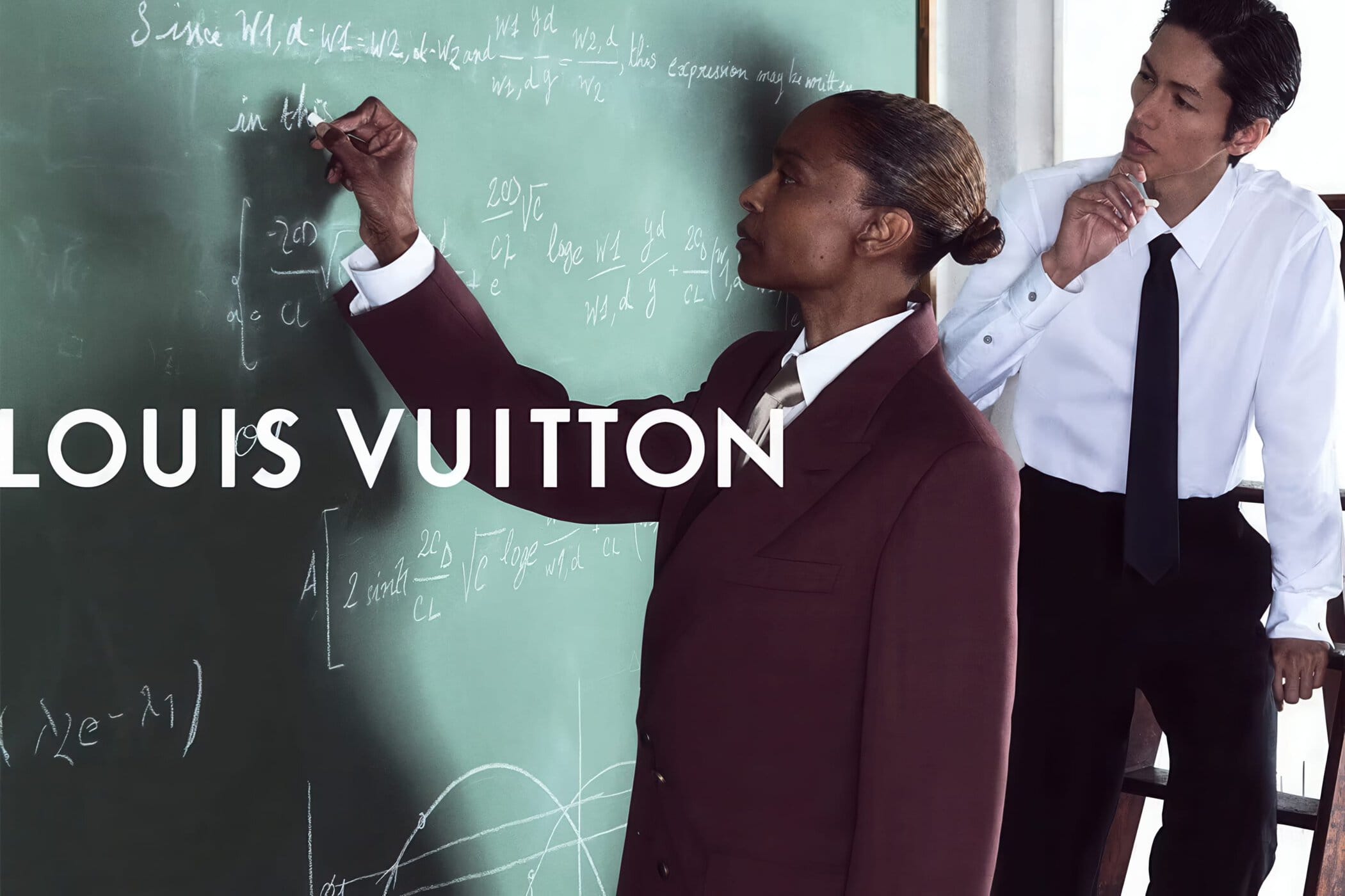 Two models posing in front of a green chalkboard covered in chalk equations for Louis Vuitton Men's Fall 2026 campaign.
