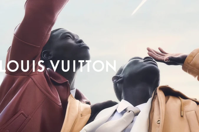 Two Black male models looking upward wearing leather jackets and tailored menswear against an open sky for Louis Vuitton.